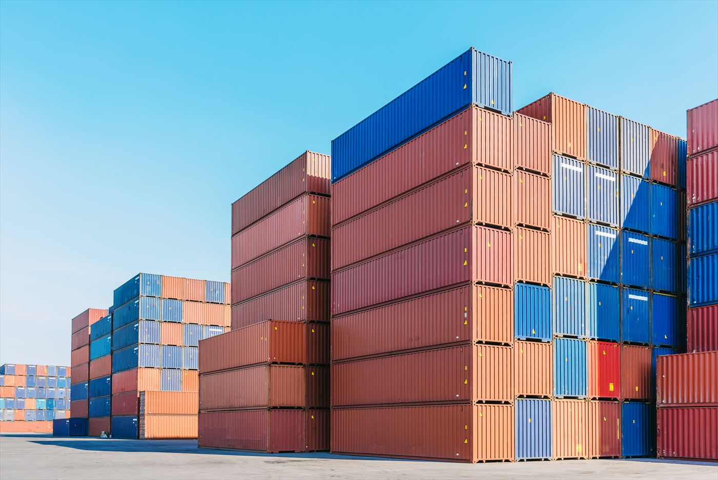 Stacked shipping containers at a port yard under a clear sky